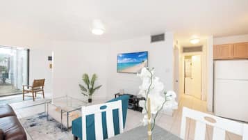 A modern living room with a glass partition, a dining area with a table and chairs, a sofa, a potted plant, and a painting on the wall.