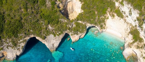 An aerial view of a coastal area with clear turquoise waters, rocky cliffs, and dense greenery.