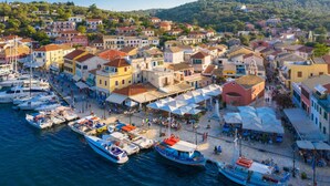 A coastal town with colorful buildings, a marina with boats, and outdoor seating areas. - Villa Alkyon in Paxi (Paxos)