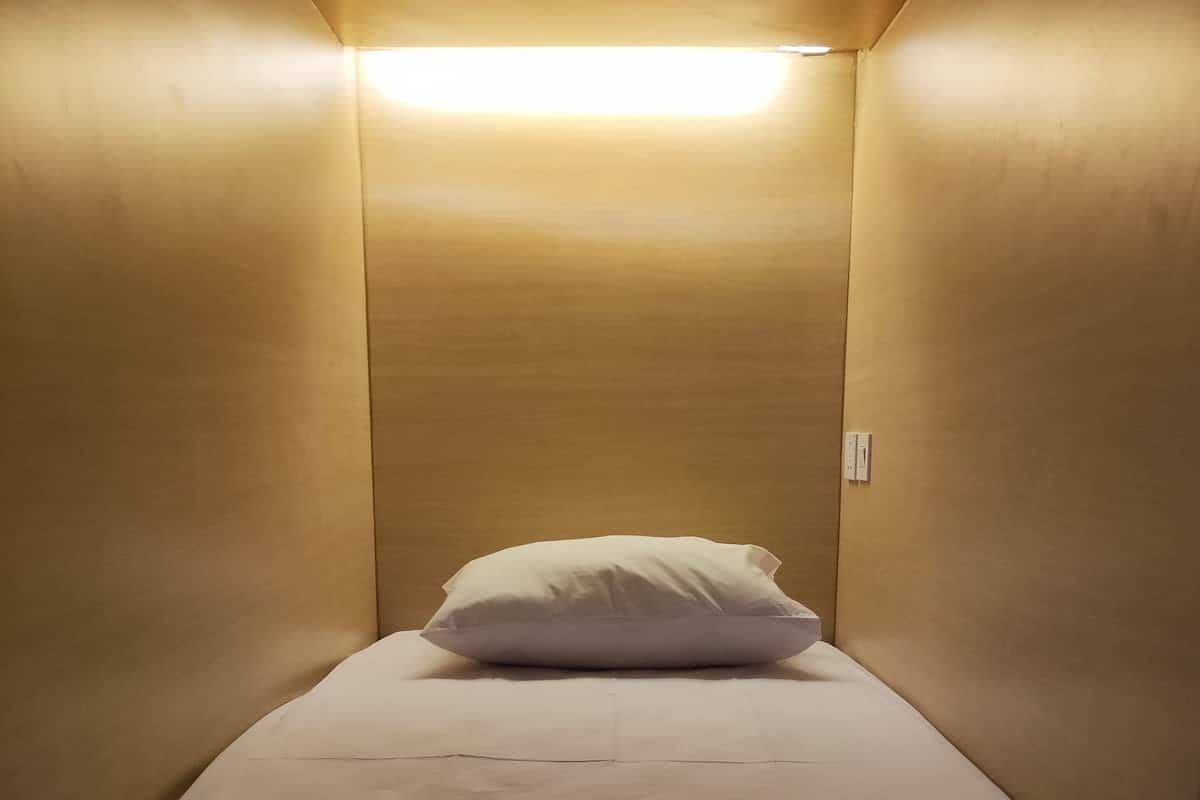 A small, dimly lit room with a single bed and a white pillow.