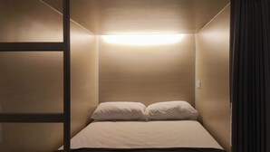 A small, single-bed room with a slanted ceiling and a single overhead light.