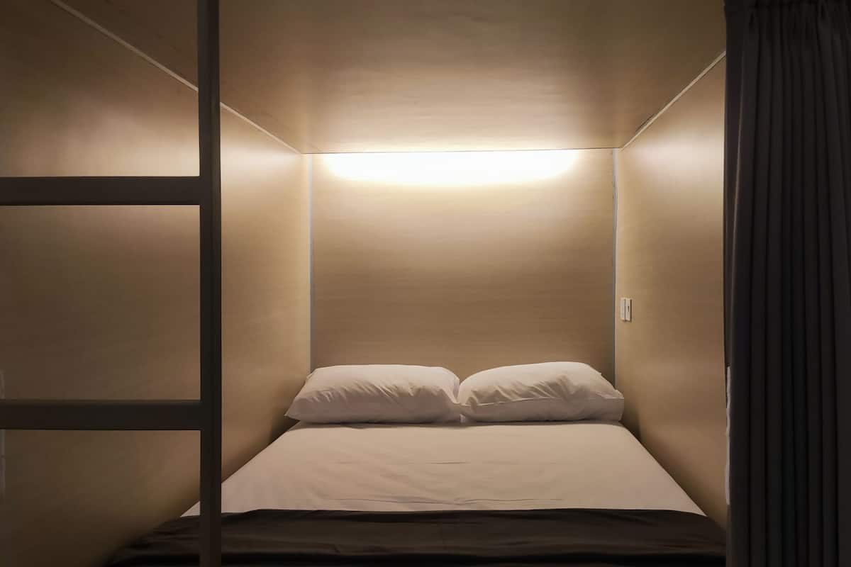 A small, single-bed room with a slanted ceiling and a single overhead light.