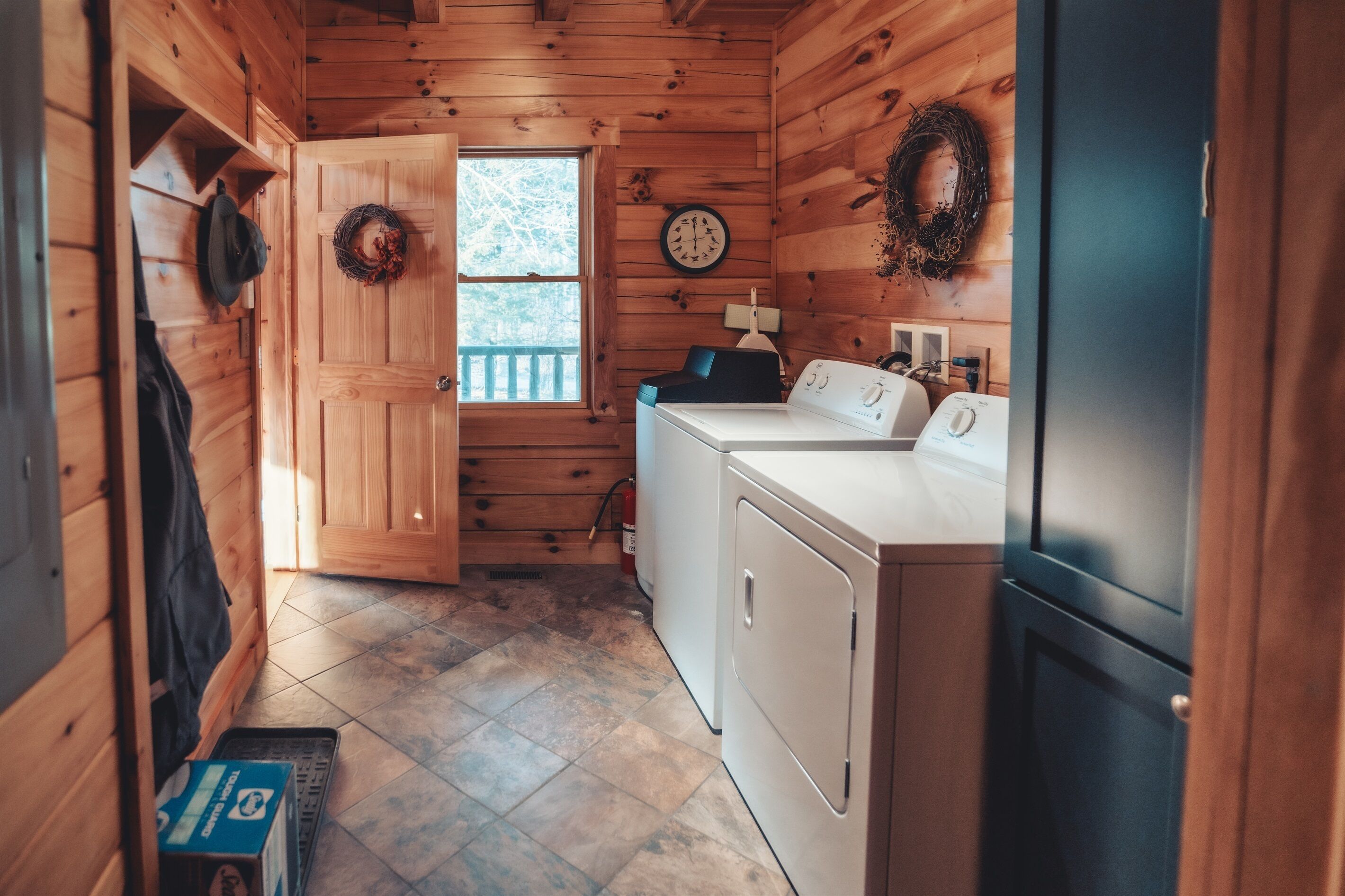 A laundry room with wooden walls, a washing machine, a dryer, and a clock on the wall.