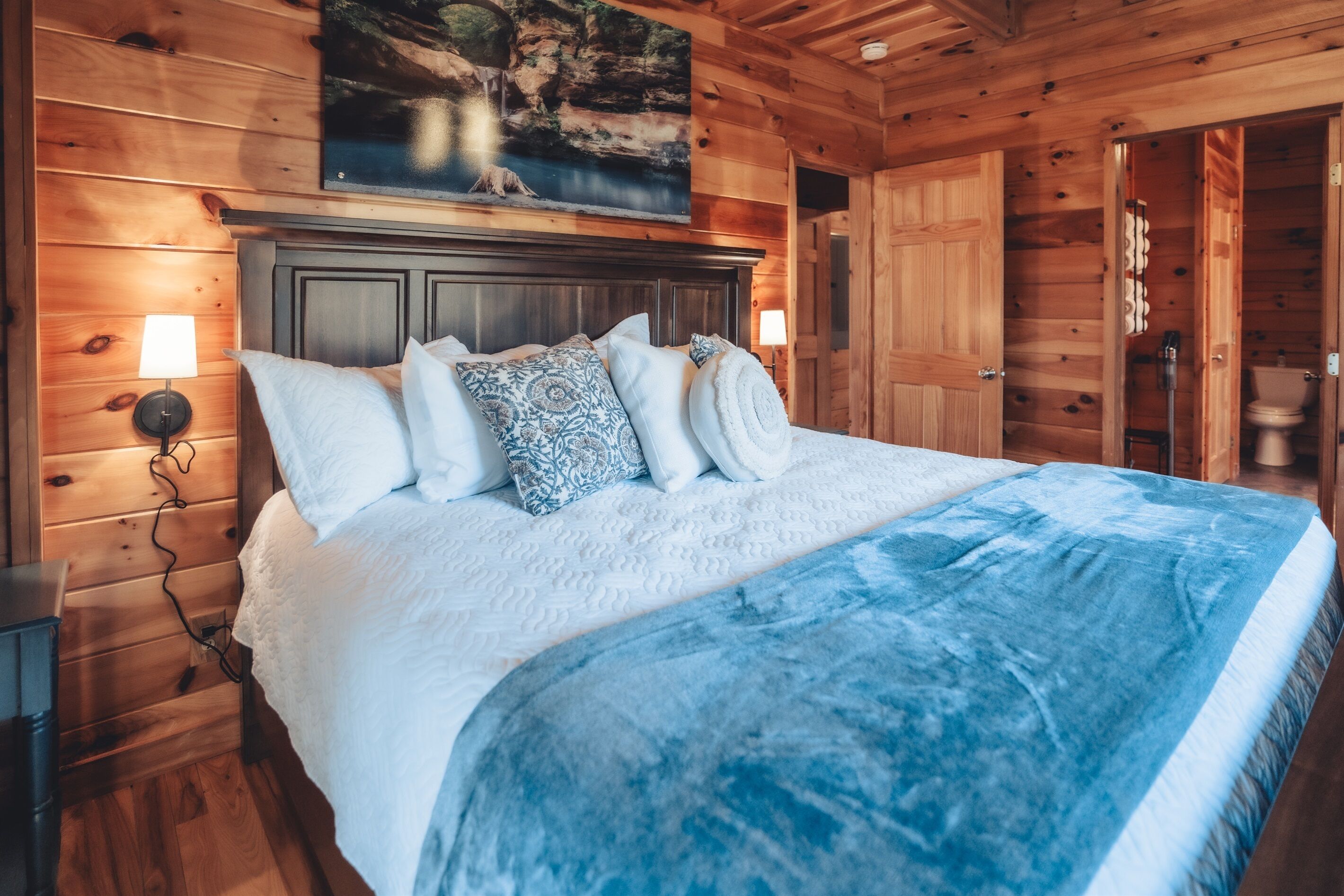 A wooden cabin bedroom with a bed, pillows, and a painting above the bed.