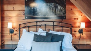 Una cama con ropa de cama blanca y gris, dos lámparas de noche y un cabecero de madera.