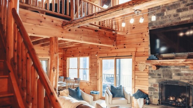 Un interior espacioso de cabaña de madera con escalera de madera, chimenea y una zona de estar acogedora.