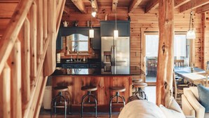 Interior de una cabaña de madera con cocina, taburetes de bar y comedor.