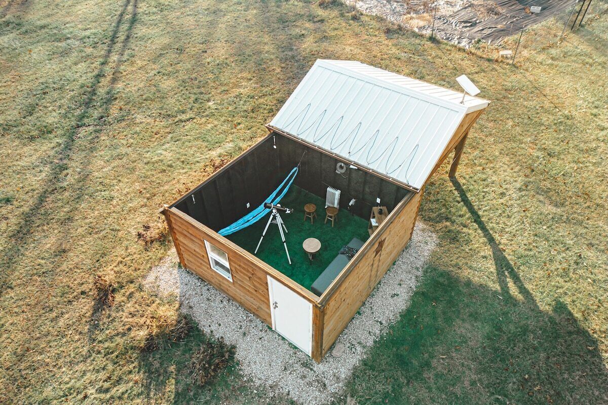 A wooden cabin with a metal roof, a telescope, and a small dining area.
