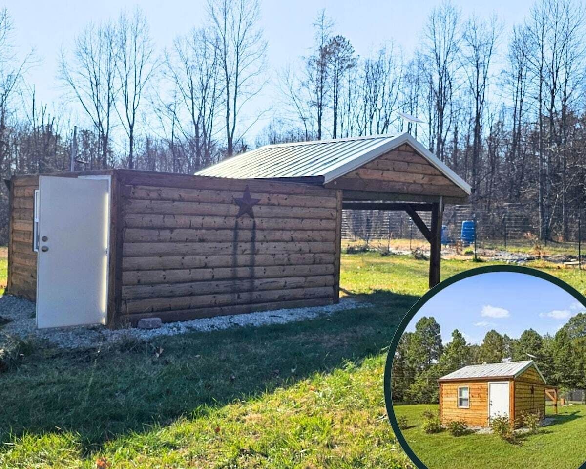 A wooden cabin with a metal roof, a small attached shed, and a clear view of a forested area in the background.