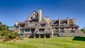 A large, multi-story building with a prominent clock tower, multiple balconies, and a well-maintained lawn. - Mt Green 3-F04 | Studio Condo (Killington)