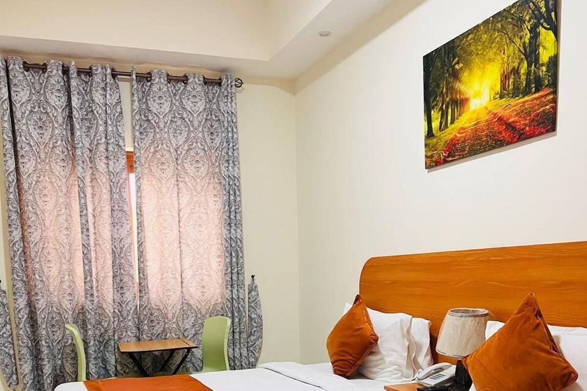 Une chambre d’hôtel avec deux lits, une tête de lit en bois, un tableau représentant une forêt et une petite table avec une lampe.