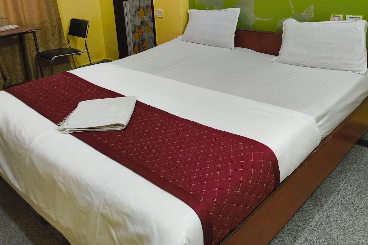 Habitación de hotel con una cama grande, colcha de patchwork roja, almohadas blancas y una pared verde con diseños de hojas.