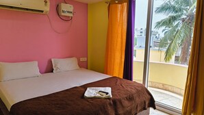 Una habitación de hotel con una cama, un equipo de aire acondicionado, una ventana con cortinas y vistas a palmeras.