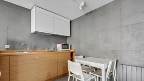 A modern kitchen with a wooden countertop, white cabinets, a white dining table with chairs, and a microwave.