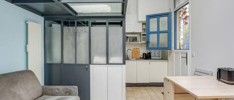 Ein kompakter Wohnbereich mit Sofa, einem kleinen Holztisch, einer Küchenzeile und einer Glastür zum Balkon.
