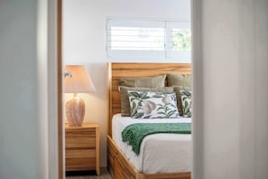 Ein Schlafzimmer mit einem Holz-Kopfteil, einem Nachttisch mit Lampe und einem Fenster mit Jalousien.