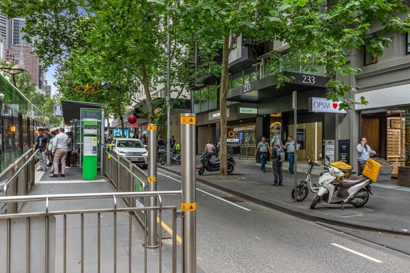 Une scène de rue avec un arrêt de tramway, un immeuble portant le numéro 233 et une vitrine ornée d’un symbole en forme de cœur.