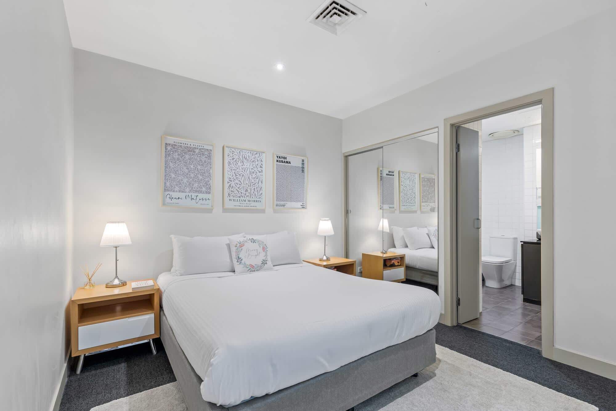 Une chambre d’hôtel moderne, dotée d’un grand lit, de tables de chevet, d’un miroir et d’œuvres d’art accrochées aux murs.