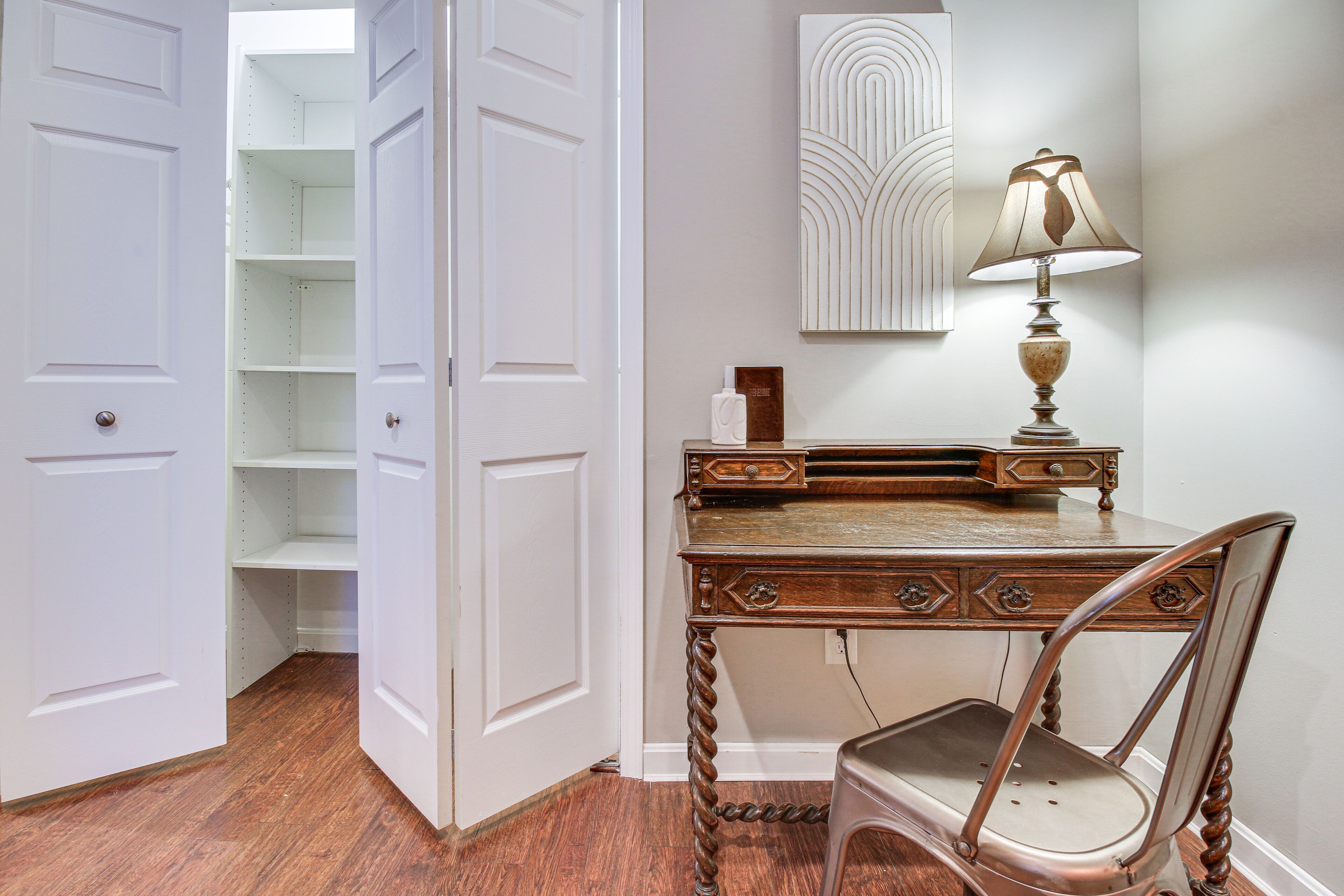 A room with a wooden desk, a chair, a lamp, and a white door leading to a closet.