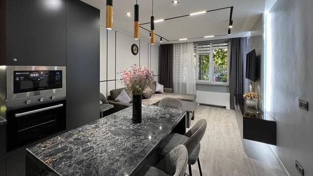 Une cuisine moderne dotée d’un plan de travail en marbre, d’un four encastré et de luminaires suspendus.