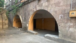 Un bâtiment en pierre doté de deux portes en arc de cercle, d’un sol en béton et d’une grille métallique.