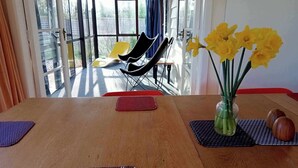 Un comedor con una mesa de madera, un florero con flores amarillas y vistas al exterior a través de amplias ventanas.