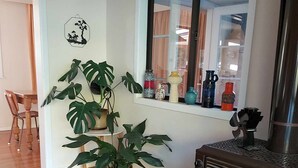 Una sala de estar con piso de madera, una planta en maceta, un ventanal con adornos y un estufa de leña.