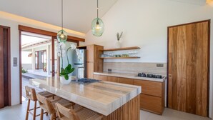 Une cuisine moderne dotée d’un grand îlot central, de tabourets de bar en bois et d’un luminaire suspendu.
