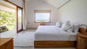 Une chambre dotée d’un grand lit, d’une tête de lit en bois, d’une table de chevet, d’une fenêtre offrant une vue agréable et d’une porte-fenêtre coulissante donnant sur un balcon.