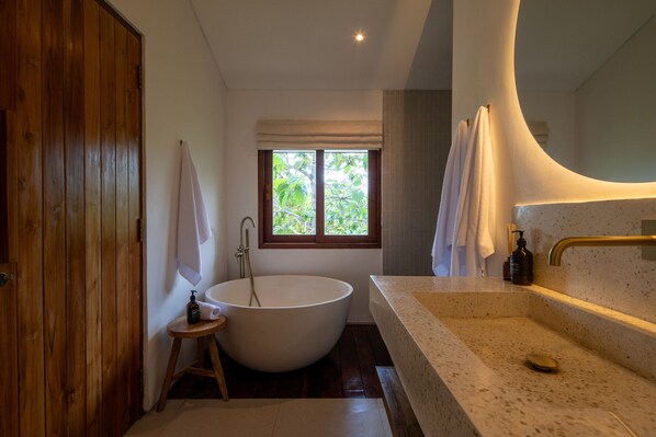 A bathroom with a freestanding bathtub, a sink with a countertop, and a window with a view of greenery.
