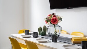 Una mesa de comedor con un florero, dos tazas negras y un cactus sobre un mantel blanco.