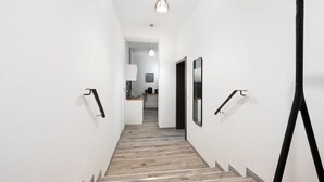 Una escalera moderna con escalones de madera y barandillas negras, que conduce a una habitación luminosa con techo blanco y una lámpara colgante.