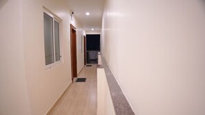 Un pasillo estrecho y bien iluminado con suelo de madera y paredes blancas, que conduce a una habitación oscura al final.