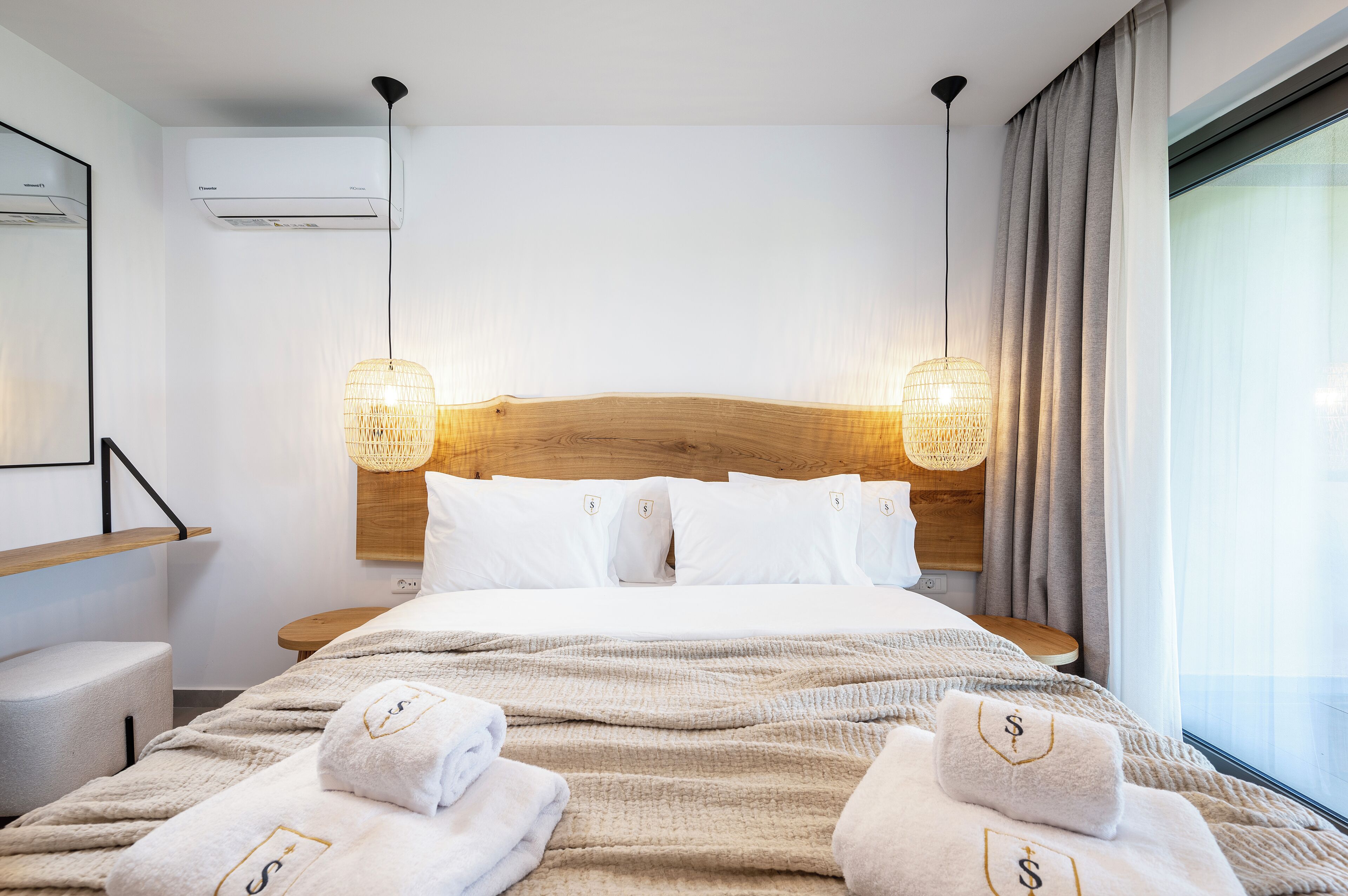 A modern hotel room with a large bed, two bedside lamps, a wooden headboard, and a large window with curtains.