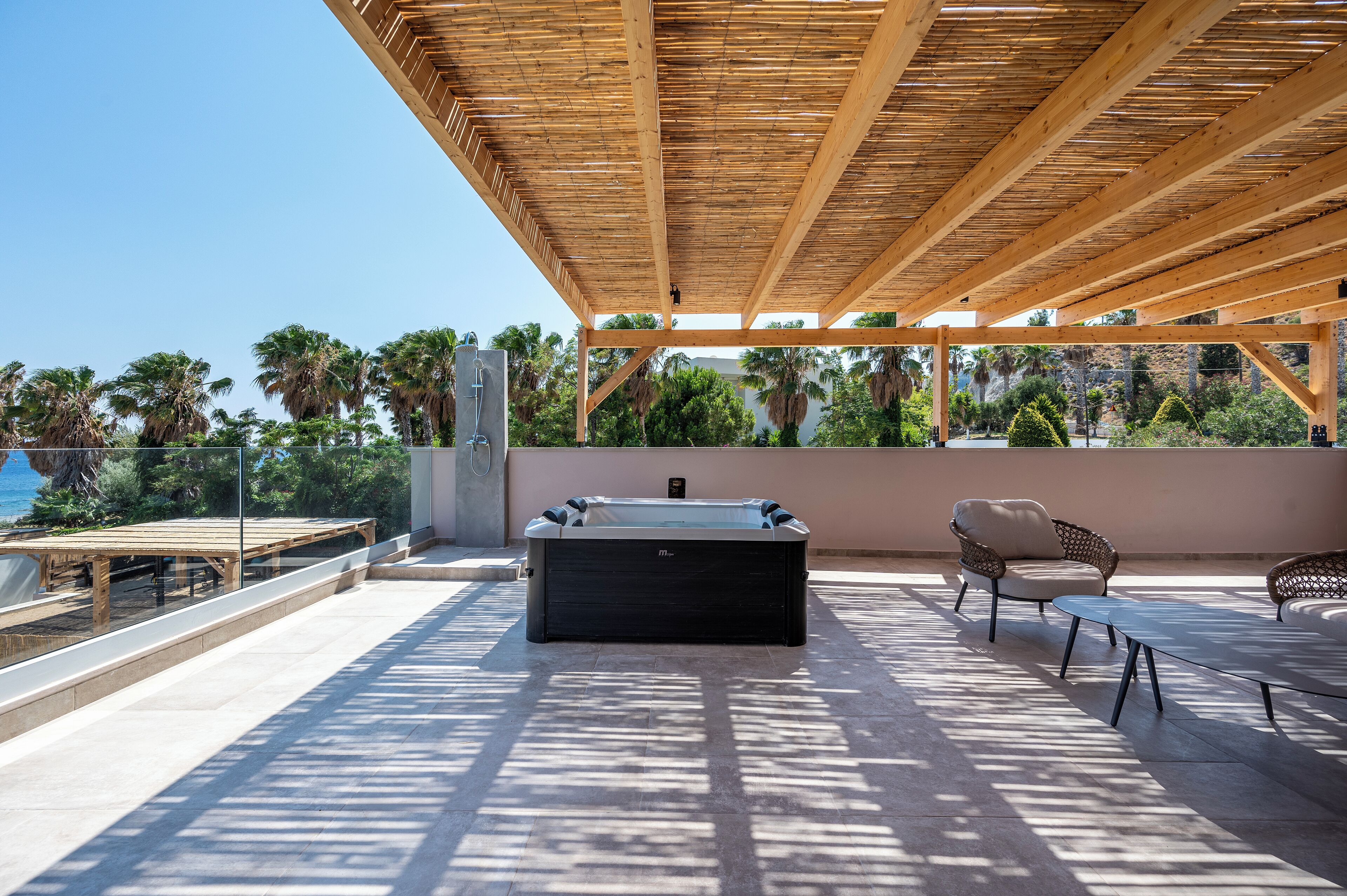 A rooftop patio with a hot tub, seating area, and a view of palm trees and mountains.