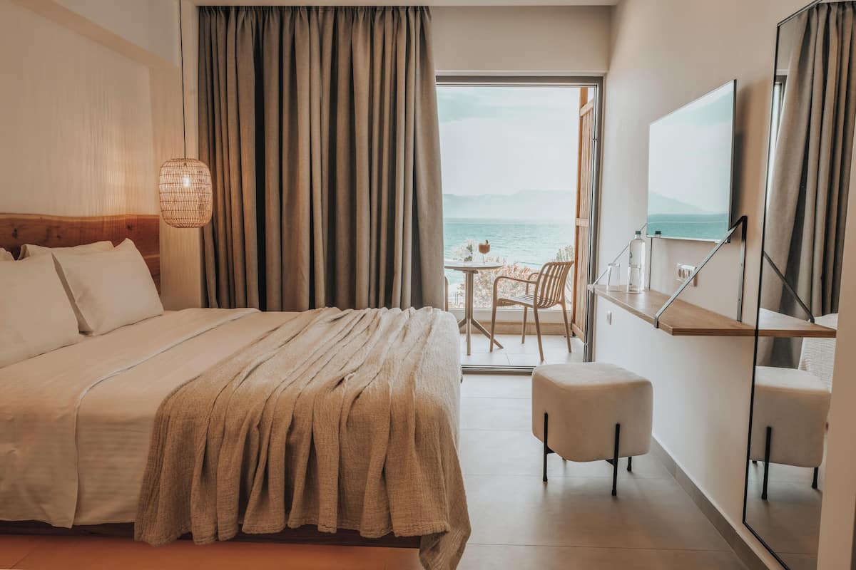 A hotel room with a bed, a small table with chairs, a TV, and a view of the sea.