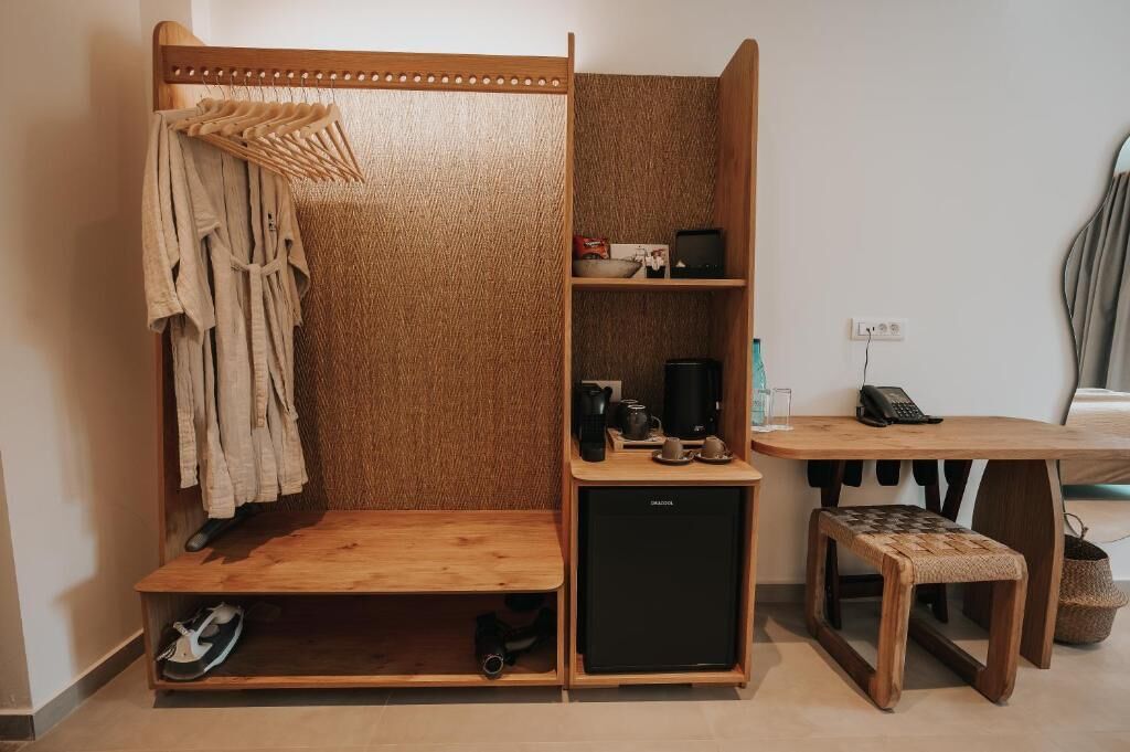 A compact room with a wardrobe, a small kitchenette, a desk, and a bench.