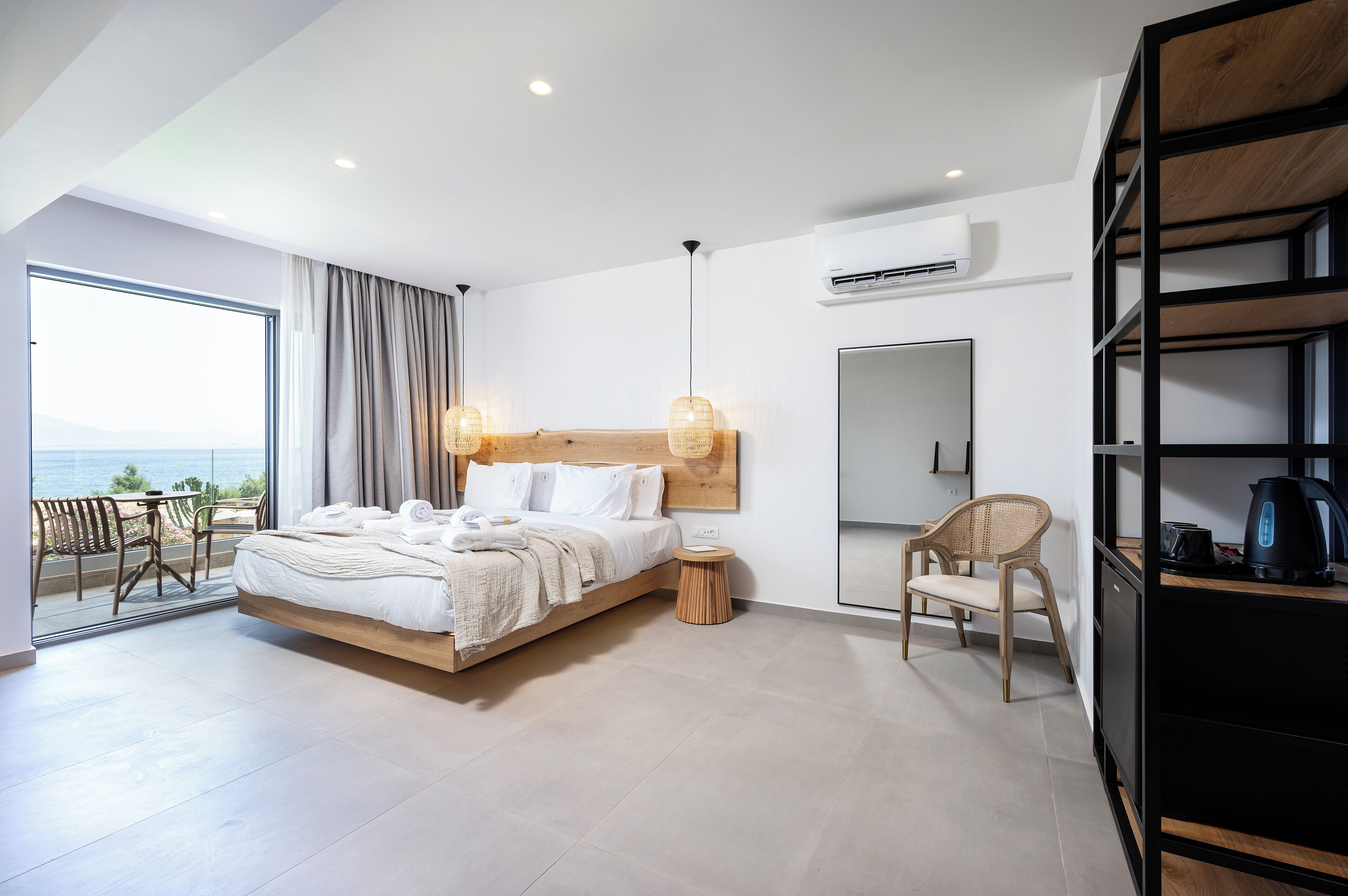 A modern bedroom with a large bed, a view of the sea, a dining area, and a kitchen area.