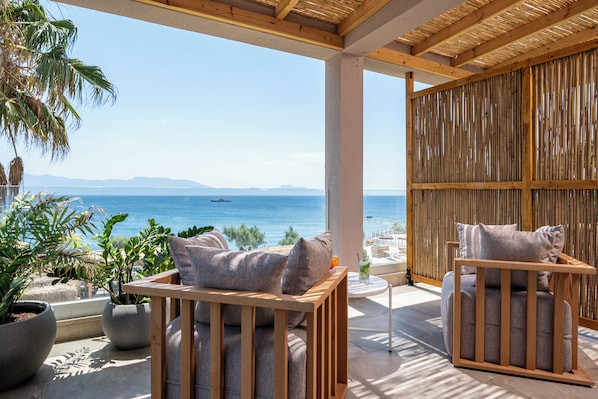 A terrace with two wooden-framed sofas, a potted plant, and a view of the sea. - Sagredo Beachfront Retreat & Spa by E-GEO (Kos)
