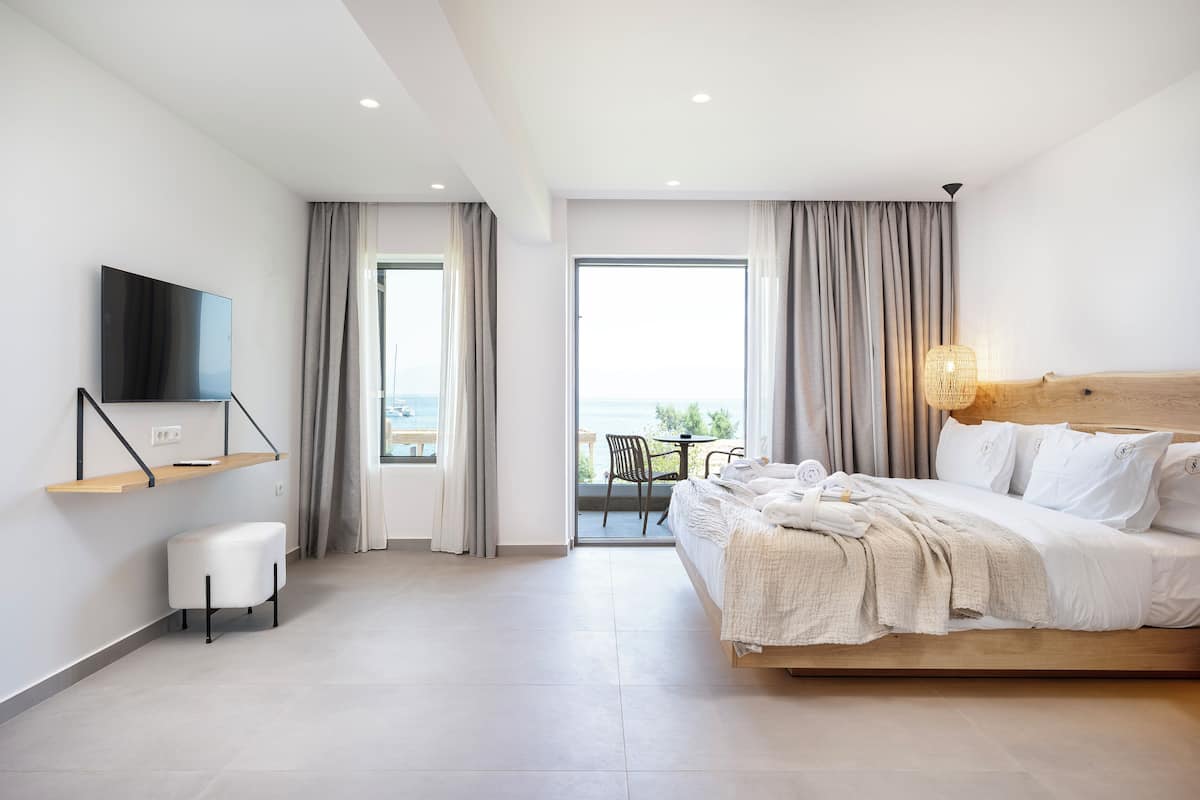 A modern hotel room with a large bed, a TV mounted on the wall, a small seating area, and a balcony with a view.