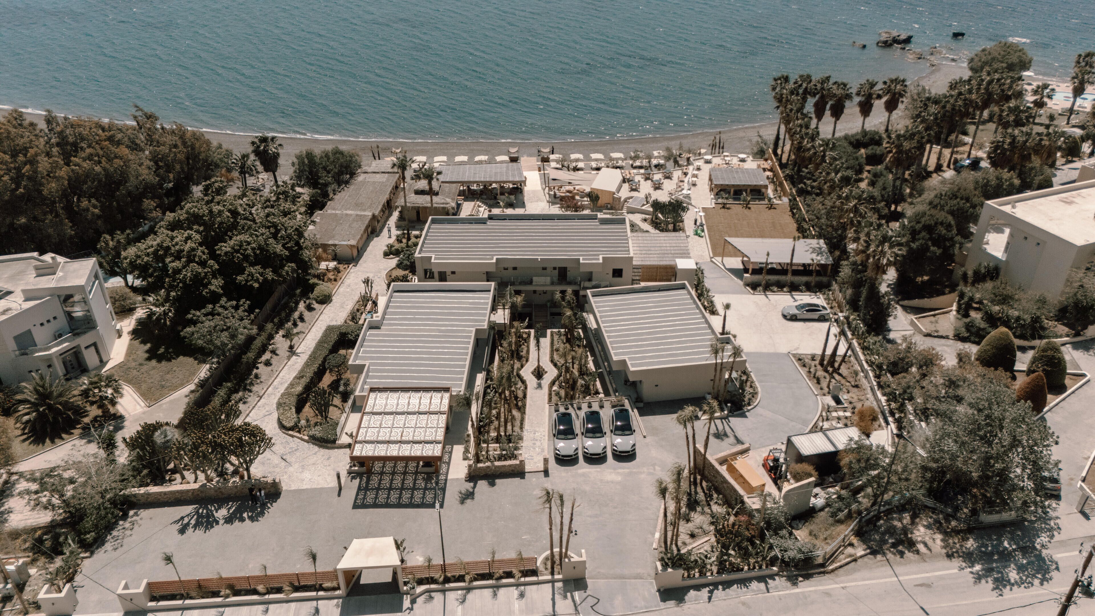 An aerial view of a hotel with a central courtyard, multiple parking spaces, and a beach in the background.