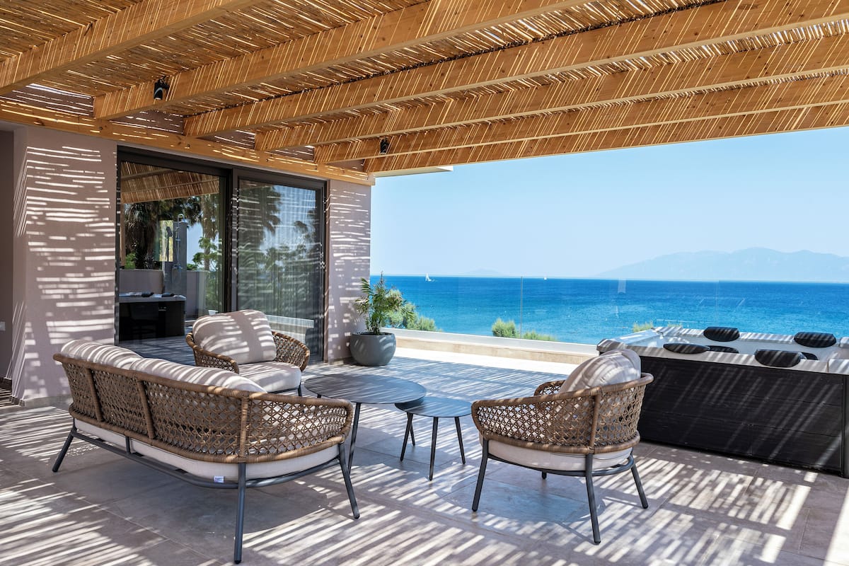 A covered outdoor seating area with wicker furniture and a view of the sea.