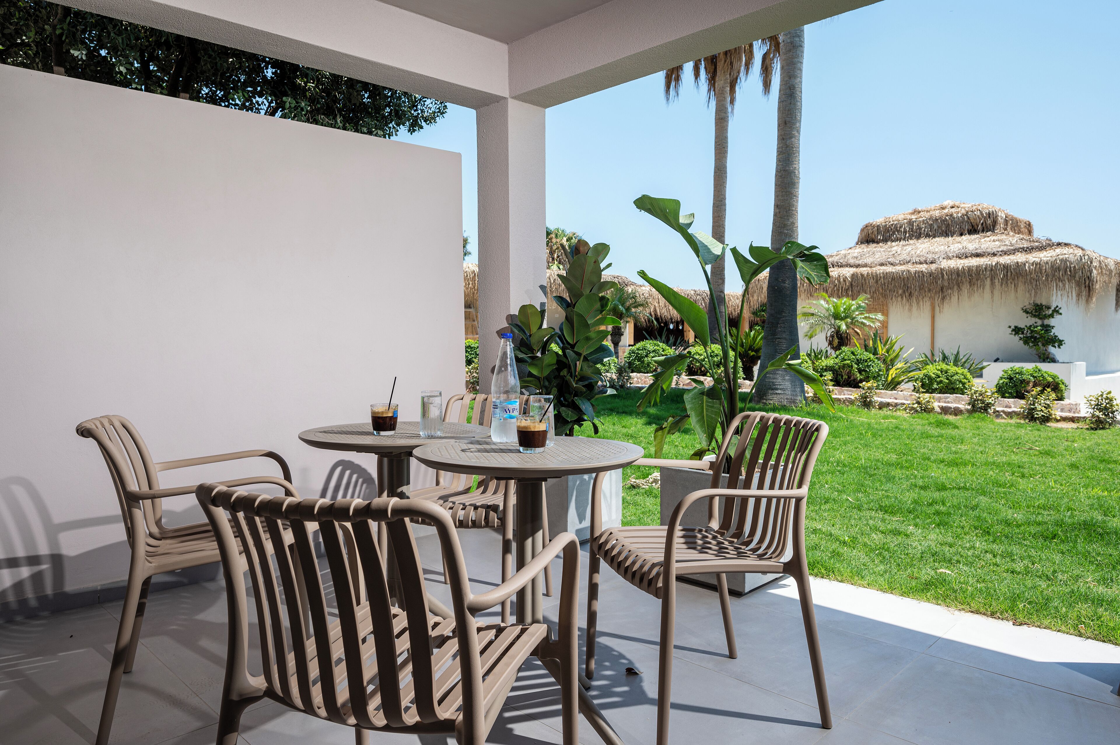 Un patio con una mesa y sillas, una botella de agua y un vaso de una bebida oscura.
