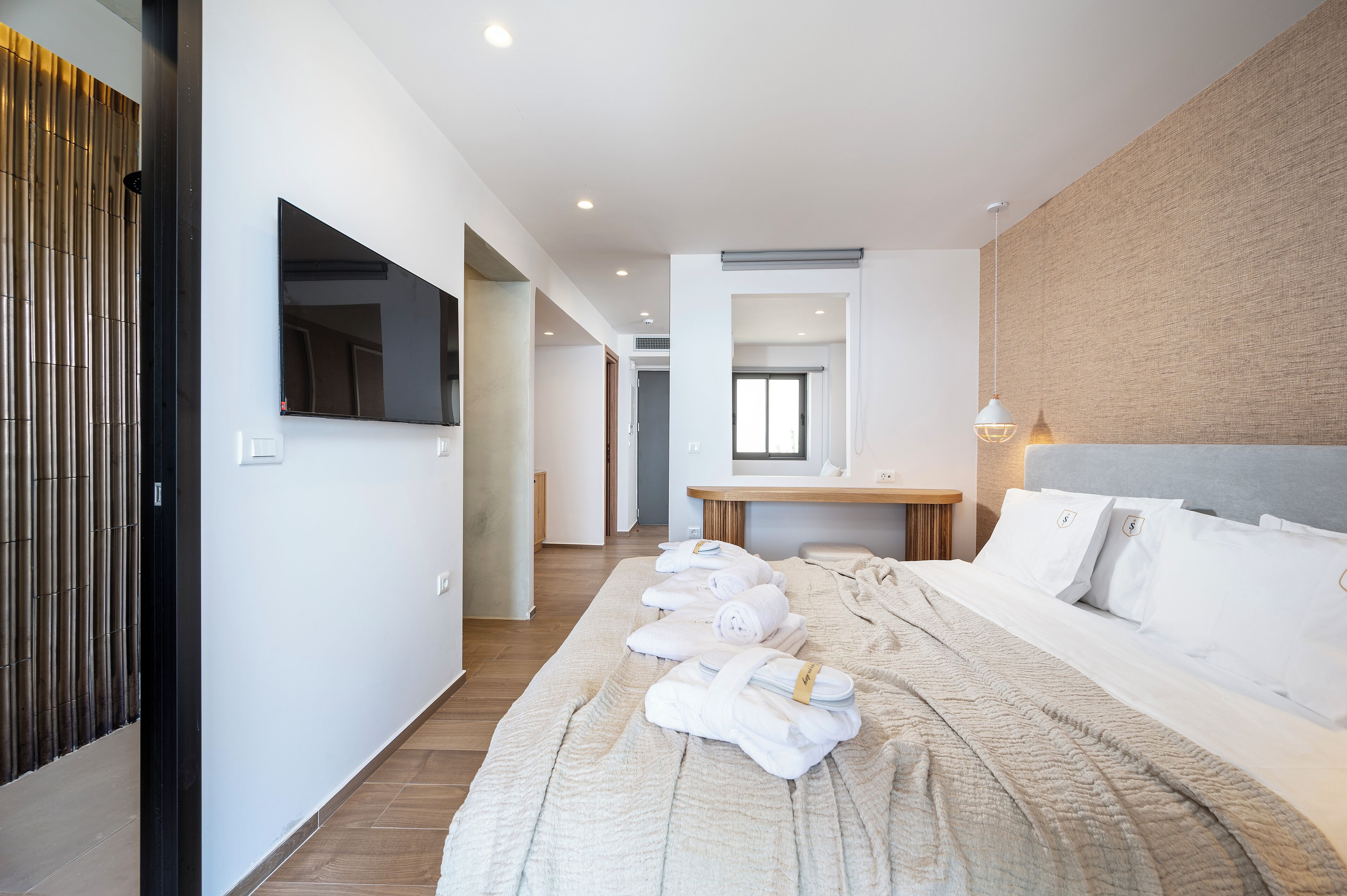 A modern hotel room with a large bed, a flat-screen TV, a wooden side table, and a view of the hallway.