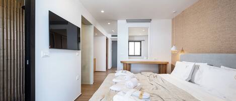 A modern hotel room with a large bed, a flat-screen TV, a wooden side table, and a view of the hallway.