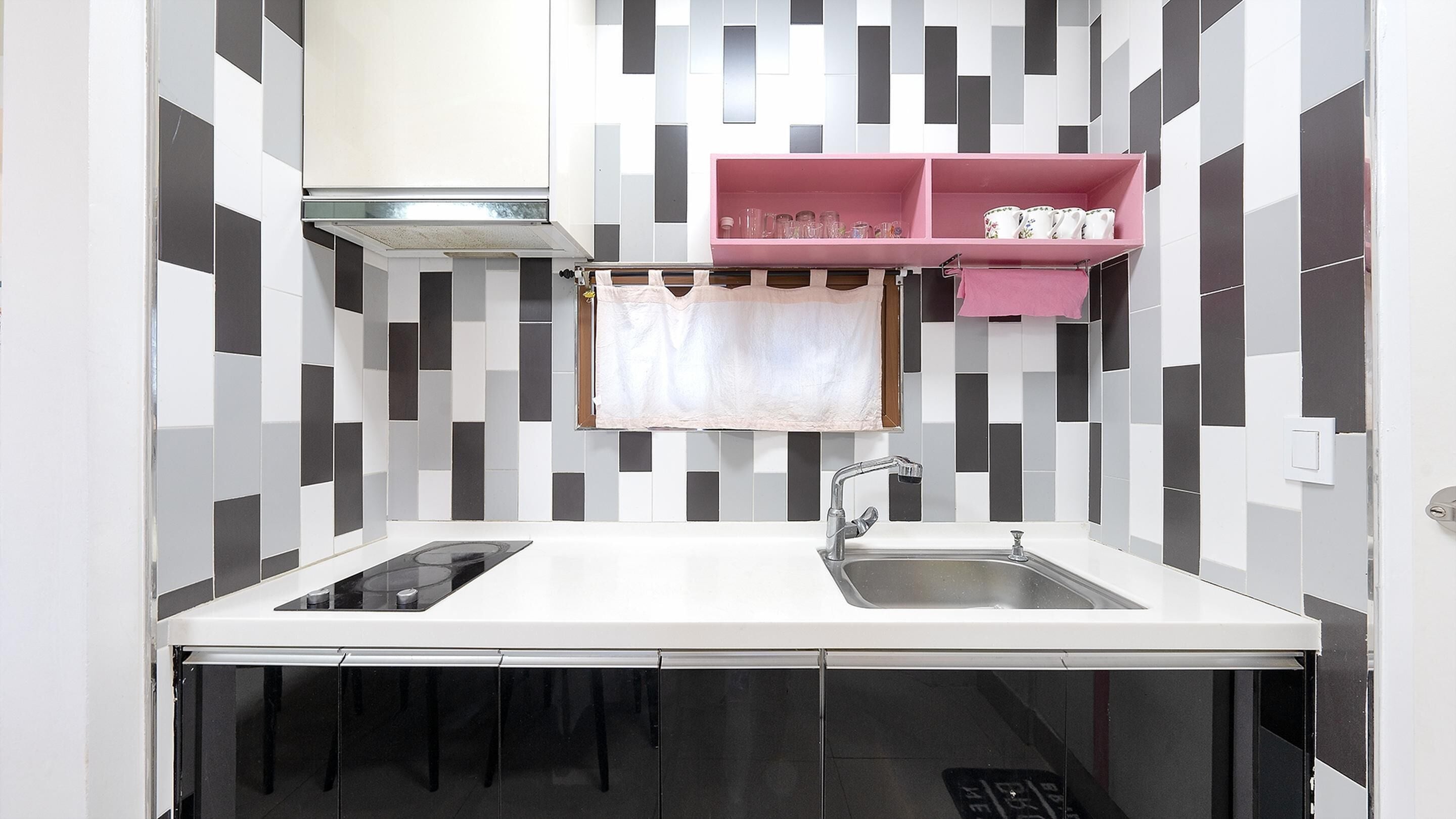 A compact kitchen with a white countertop, a stainless steel sink, and a pink shelf above it.