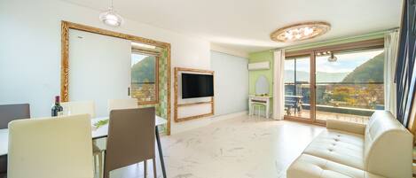 A modern living room with a large window, a flat-screen TV, a sofa, and a dining area with chairs and a table.