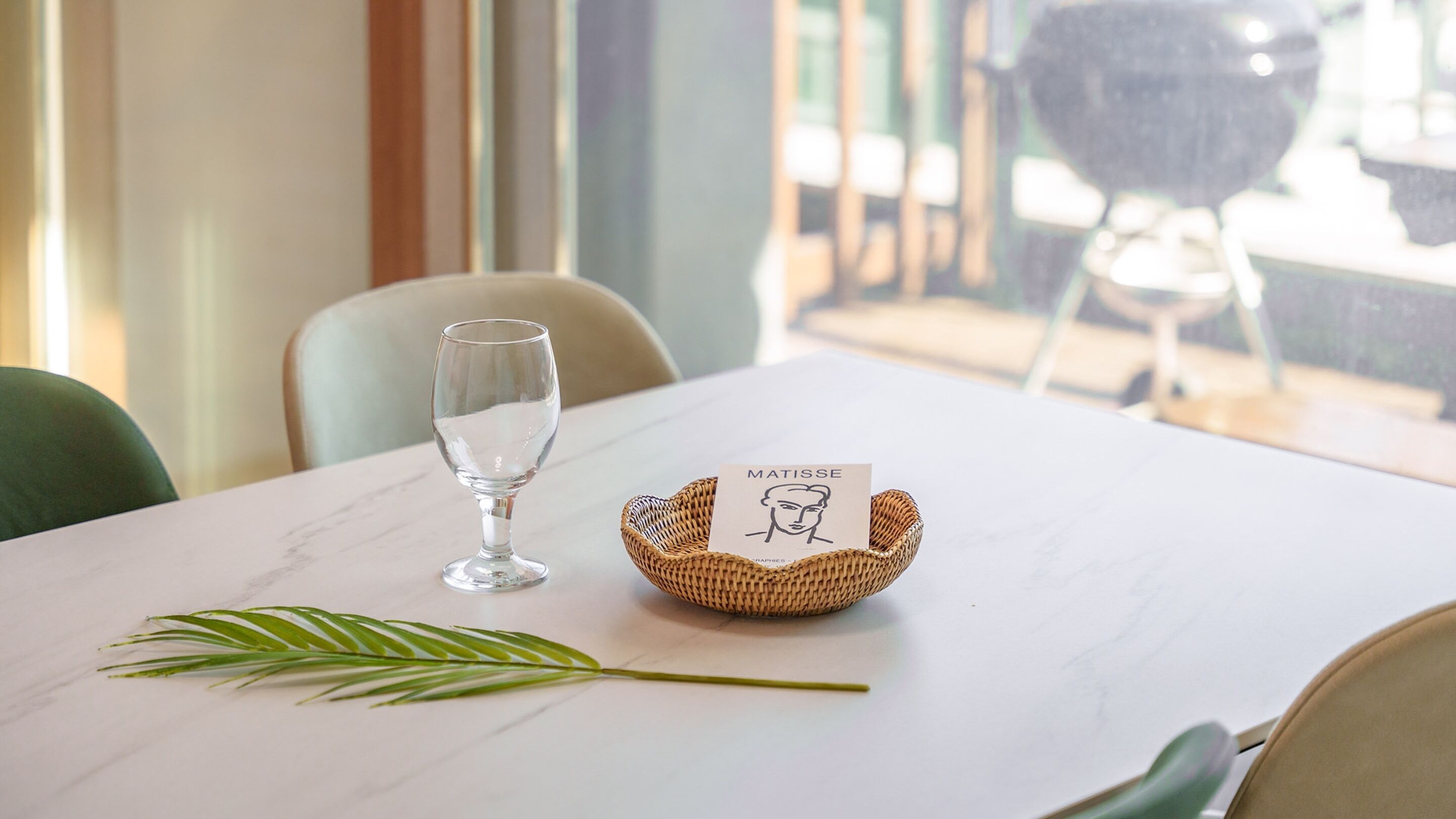 A table with a clear glass, a woven basket with a card, and a green plant.