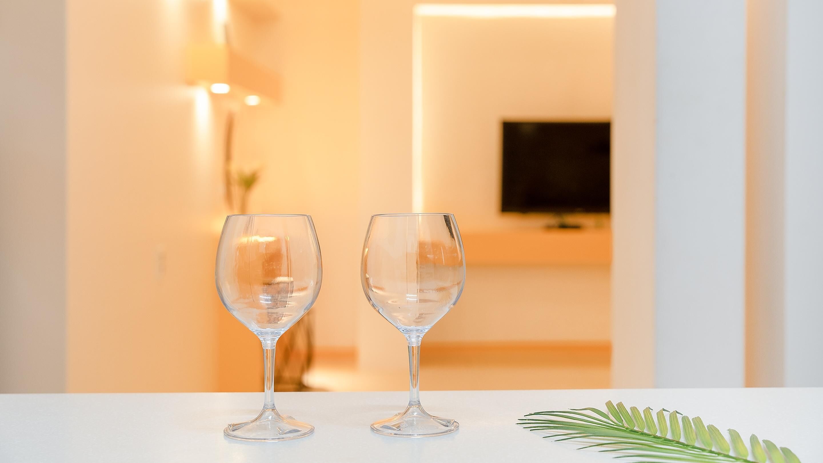Two empty wine glasses on a white table with a green plant beside them.