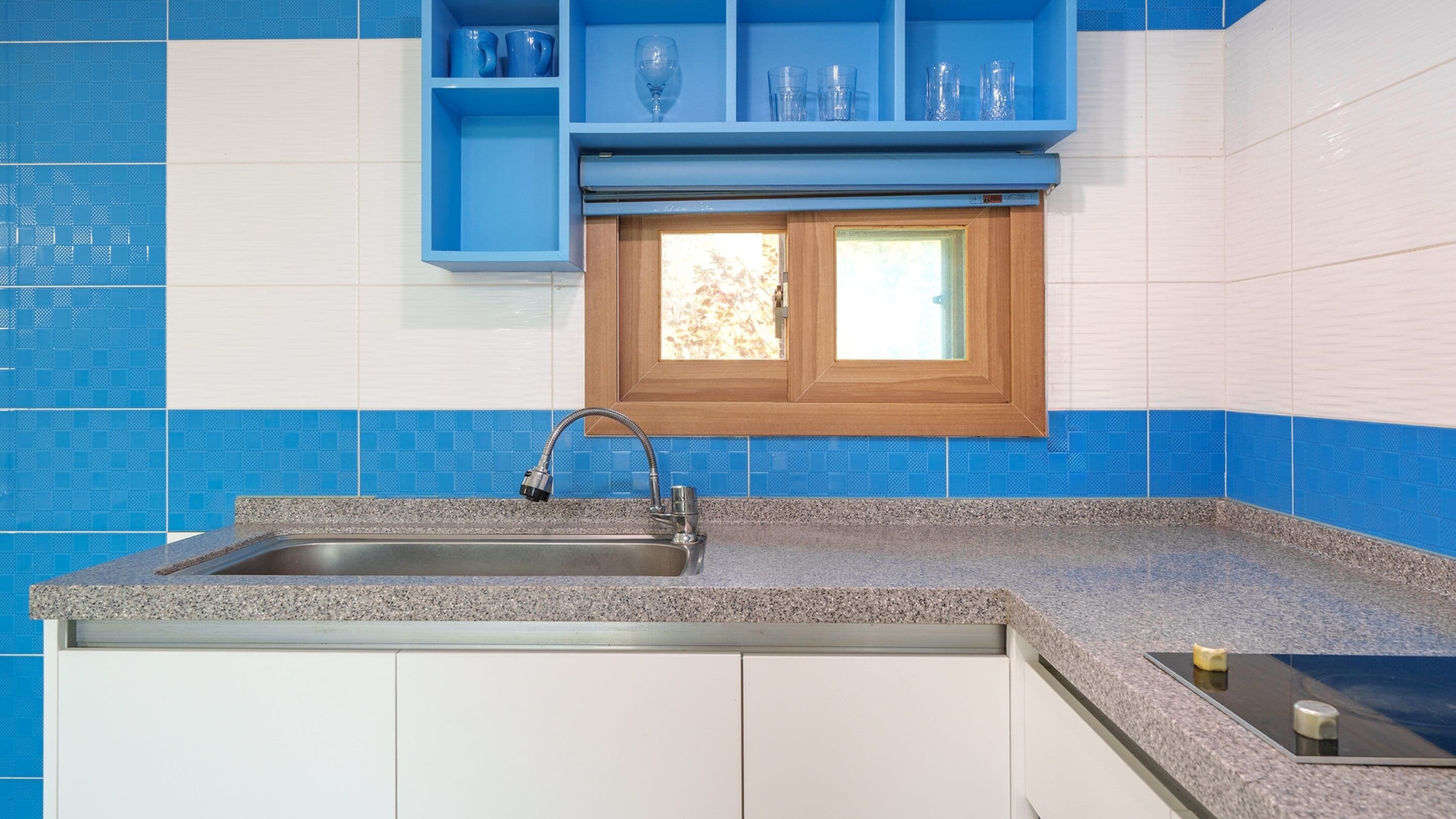 A kitchen with a granite countertop, a stainless steel sink, and blue and white tiled backsplash.